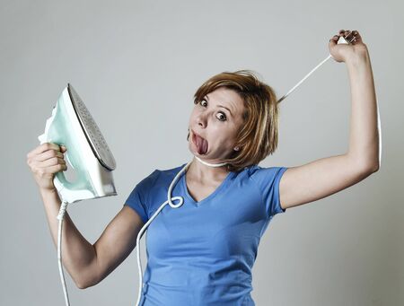 young crazy stressed housewife or maid domestic service woman holding upset an iron strangling her neck with cable tired overworked and bored in housework housekeeping and cleaning conceptの写真素材