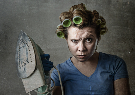 young attractive woman or housewife sad bored and stressed holding iron angry and frustrated in domestic work housekeeping and housework concept isolated grunge dirty backgroundの写真素材