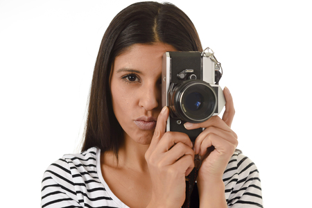 young attractive latin woman taking pictures looking through the viewfinder of an cool retro and vintage photographic camera smiling happy in photography hobby and learning pro photo shootingの写真素材