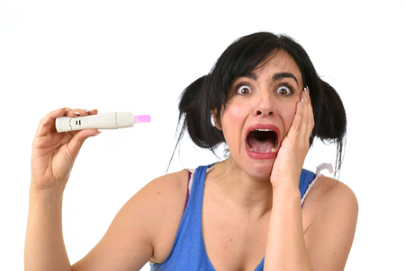 young pregnant woman scared in shock checking pink positive result on pregnancy test surprised and stressed in accidental motherhood and unwanted baby isolated on white backgroundの写真素材