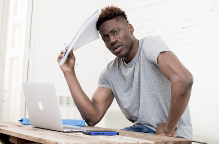 young attractive african american man sitting at home living room working with laptop computer and paperwork looking stressed and desperate maybe studying for exam in education conceptの写真素材