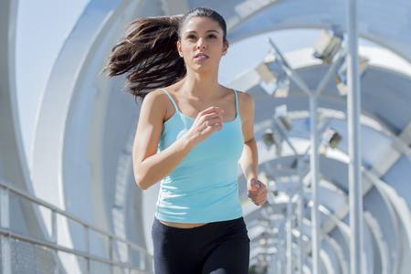 young beautiful and athletic sport woman running and jogging in urban training workout crossing modern metal city bridge in female runner body care and healthy lifestyle conceptの写真素材