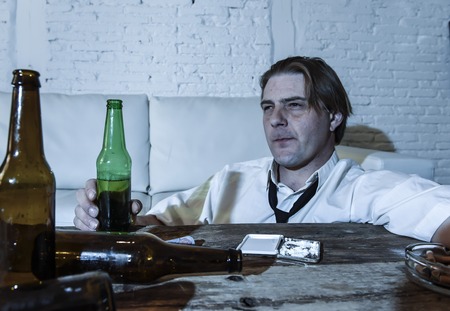 wasted alcoholic and drug addict man with loose tie snorting cocaine and drinking beer bottles at home living room couch in toxic substance addiction and abuse conceptの写真素材