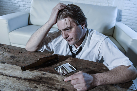 wasted alcoholic and drug addict man with loose tie snorting cocaine and drinking beer bottles at home living room couch in toxic substance addiction and abuse conceptの写真素材