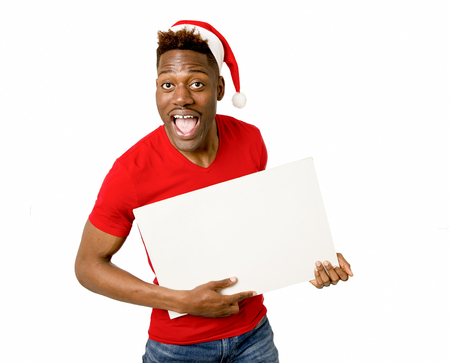 young attractive black afro american man in Christmas Santa hat smiling happy and showing blank billboard with copy space for adding xmas advertising text isolated on white in sales and offer conceptの写真素材