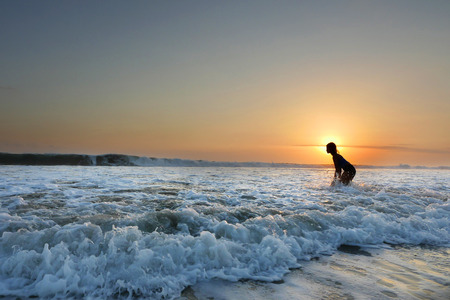 young beautiful Asian girl alone at sea shore looking at orange sky sunset over ocean at Indonesia...