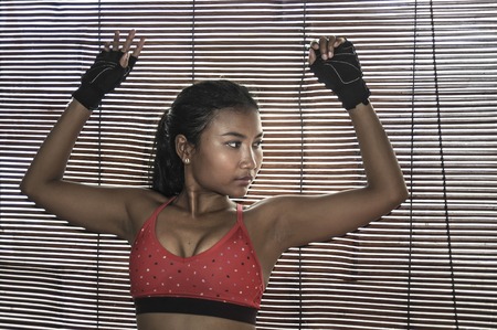 shady portrait of young beautiful Asian woman in gym sport cloths posing in Venetian blinds...