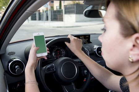 close up hand of woman holding steering wheel and blank screen mobile phone driving car while...