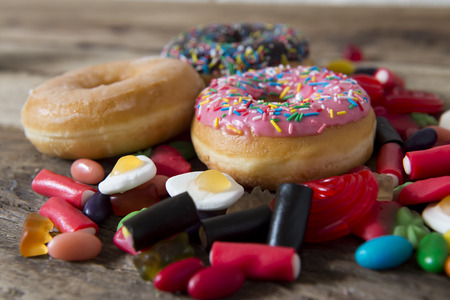 unhealthy but delicious group of sweet sugar donut cakes and lots of gummy candies on vintage wooden table in lifestyle nutrition health care and calories abuse and dieting conceptの写真素材
