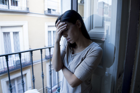 young sad and desperate Latin woman at home balcony looking destroyed and depressed suffering depression feeling lonely unhappy and hopeless in mental health and crisis conceptの写真素材