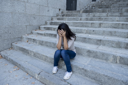 young beautiful and sad Hispanic woman desperate and depressed sitting on urban city street staircase looking confused and lost in life problems and depression conceptの写真素材