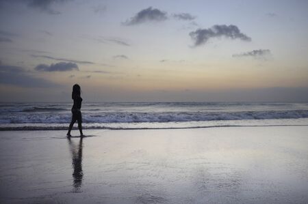 silhouette of beautiful and attractive african american black woman walking on sunset beach enjoying water and sand relaxed and happy in holiday trip and summer vacation tourism conceptの写真素材
