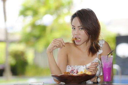 young beautiful and happy Asian woman on her 20s enjoying healthy food for brunch breakfast or lunch sitting outdoors at holiday resort coffee shop drinking fruit juice in body care and lifestyle conceptの写真素材