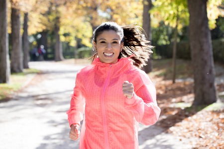 young attractive and happy runner woman in Autumn sportswear running and training on jogging outdoors workout in city park with trees and yellow leaves in fitness and healthy lifestyle conceptの写真素材