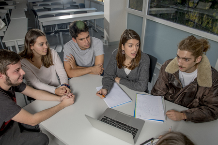 group of young male and female teenager university students at school sitting on classroom learning and working on project together with laptop computer smiling happy in uni education conceptの写真素材