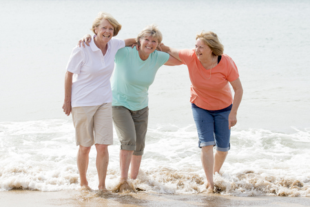 lovely group of three senior mature retired women on their 60s having fun enjoying together happy walking on the beach smiling playful in female friendship and girlfriends on holidays conceptの写真素材