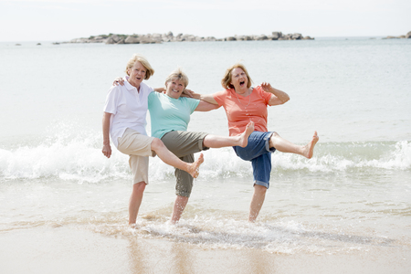 lovely group of three senior mature retired women on their 60s having fun enjoying together happy walking on the beach smiling playful in female friendship and girlfriends on holidays conceptの写真素材