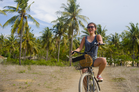 young happy and pretty Asian Chinese woman riding bike in Vietnam or Thailand tropical jungle forest with palm trees smiling relaxed in bicycle excursion and Summer holiday tourist activityの写真素材