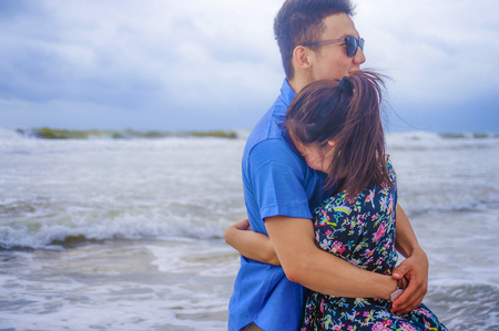 young happy and beautiful Chinese Asian couple with woman hug her boyfriend romantic and cuddle on the beach smiling in dating and romance concept celebrating Valentinesの写真素材