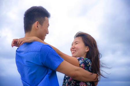 young happy and beautiful Chinese Asian couple with woman hug her boyfriend romantic and cuddle on the beach smiling in dating and romance concept celebrating Valentinesの写真素材
