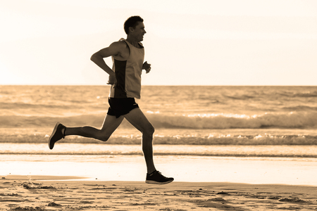 portrait of young athletic fit and strong runner man training on Summer sunset beach in sea shore running and fitness workout in sport and healthy lifestyle conceptの写真素材