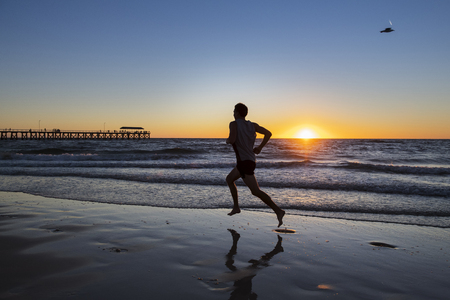 silhouette of young dynamic athlete runner man with fit strong body training on beautiful Summer sunset beach sand running barefoot in sport well being and healthy lifestyle conceptの写真素材