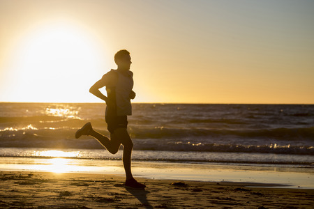 silhouette of young dynamic athlete runner man with fit strong body training on beautiful Summer sunset beach sand running barefoot in sport well being and healthy lifestyle conceptの写真素材