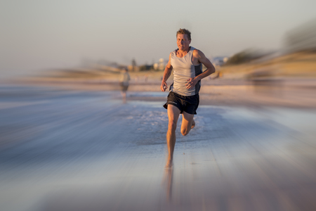 frontal portrait of young athletic fit and strong runner man training on Summer sunset beach in sea shore running and fitness workout in sport and healthy lifestyle concept with motion blur effectの写真素材