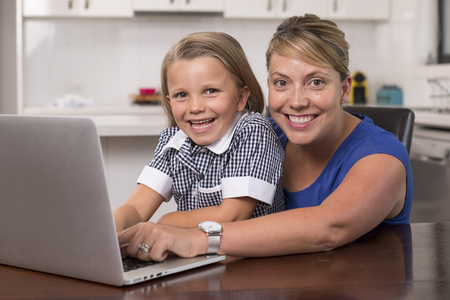 blond mother woman together with her young beautiful and sweet little girl 6 to 8 years old sitting at home kitchen enjoying with laptop computer smiling happy in lifestyle conceptの写真素材