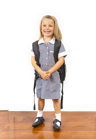 young beautiful and happy child girl 6 to 8 years old blond hair and blue eyes smiling excited wearing school uniform and backpack isolated on white background in kid education conceptの写真素材