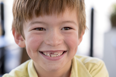 close up headshot portrait of young little 7 or 8 years old boy with sweet funny teeth smiling happy and cheerful in joy face expression looking at the camera in childhood lifestyle conceptの写真素材