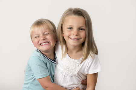 7 years old adorable blond happy girl posing with her little 3 years old brother smiling cheerful isolated on white background in children and siblings relationship conceptの写真素材