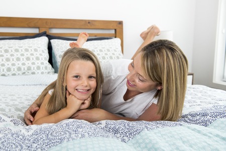 young blond Caucasian woman lying on bed together with her young sweet and adorable 7 years old daughter smiling relaxed at home bedroom in sweet mother and child lifestyle conceptの写真素材