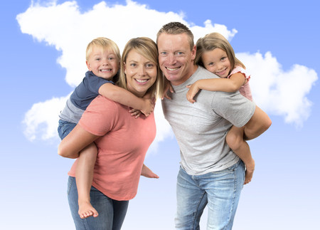 young happy and beautiful American family with husband and wife carrying on their back little son and lovely young daughter in love parents and children concept isolated on blue sky backgroundの写真素材