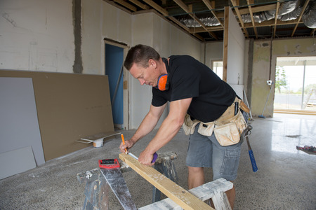 attractive and confident constructor carpenter or builder man working measuring wood with manual saw...