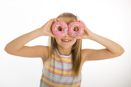young beautiful happy and excited blond girl 8 or 9 years old holding two donuts on her eyes looking through them playing cheerful in sugar calories and unhealthy sweet nutrition abuse addiction の写真素材
