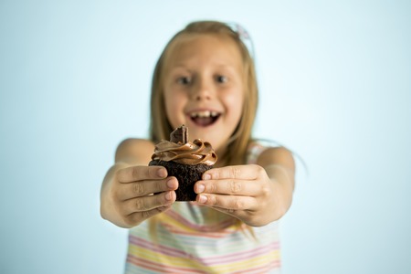 young beautiful happy and excited blond girl 8 or 9 years old holding chocolate cake on her hand looking spastic and cheerful in sugar calories and unhealthy sweet nutrition abuse addiction conceptの写真素材