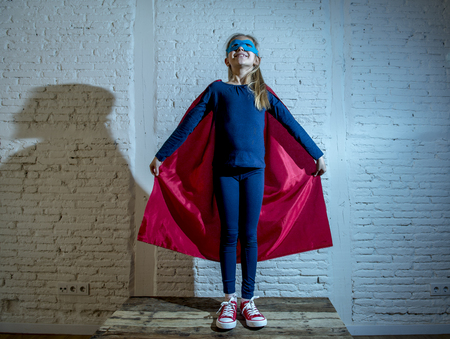 female child 7 or 8 years old young girl performing happy and excited posing wearing cap and mask in super hero fantasy costume looking playful in studio lighting dramatic setの写真素材
