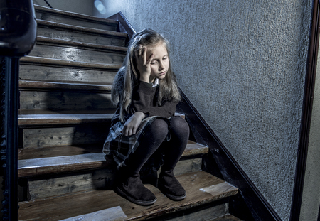 7 or 8 years old sad depressed and worried schoolgirl sitting on staircase desperate and scared suffering bullying and harassment at school in dramatic lighting and bullied children conceptの写真素材