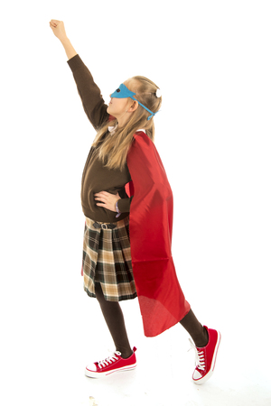 7 or 8 years old young female child in super hero costume over school uniform  performing happy and excited isolated on white background in leadership success courage and fantasy conceptの写真素材