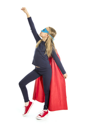7 or 8 years old young female schoolgirl child in super hero costume performing happy and excited isolated on white background in leadership success courage and fantasy conceptの写真素材