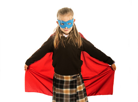 7 or 8 years old young female child in super hero costume over school uniform  performing happy and excited isolated on white background in leadership success courage and fantasy conceptの写真素材