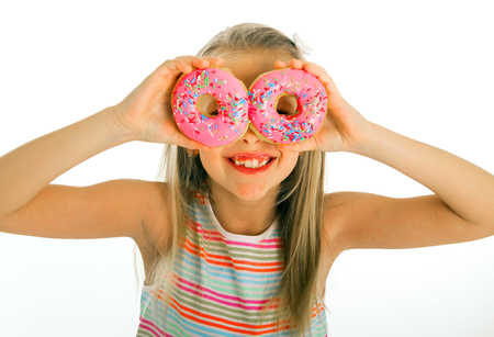 young beautiful happy and excited blond girl 8 or 9 years old holding two donuts on her eyes looking through them playing cheerful in sugar calories and unhealthy sweet nutrition abuse addiction の写真素材