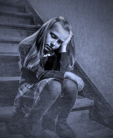 7 or 8 years old sad depressed and worried schoolgirl sitting on staircase desperate and scared suffering bullying and harassment at school in dramatic lighting and bullied children grunge editの写真素材