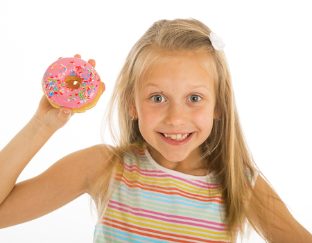 young beautiful happy and excited blond girl 8 or 9 years old holding donut on her hand looking spastic and cheerful in sugar calories and unhealthy sweet nutrition abuse addiction conceptの写真素材