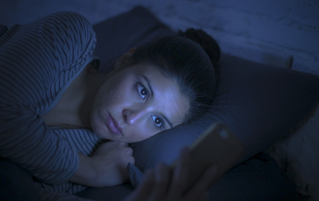 portrait of young beautiful latin woman using mobile phone late night sleepless lying in bed in the dark in smartphone and internet dating app addiction concept and communication lifestyleの写真素材