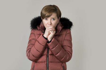 young read hair attractive and sweet woman 20s or 30s posing isolated wearing warm winter jacket with fur hood shivering and freezing feeling cold in sweet face expression の写真素材