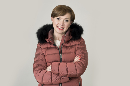 young attractive and happy red hair Caucasian woman on her 20s or 30s posing cheerful and smiling wearing warm winter jacket with fur hood isolated on grey background in seasonal fashion conceptの写真素材