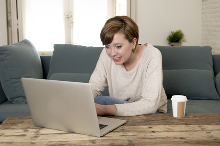 young attractive and happy woman at home sofa couch doing some laptop computer work smiling relaxed in entrepreneur lifestyle and freelance job success conceptの写真素材