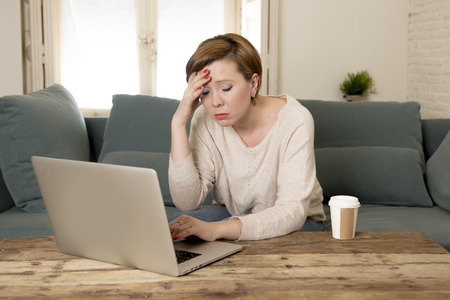 young attractive and busy woman at home sofa couch doing some laptop computer work in stress looking worried in entrepreneur lifestyleの写真素材